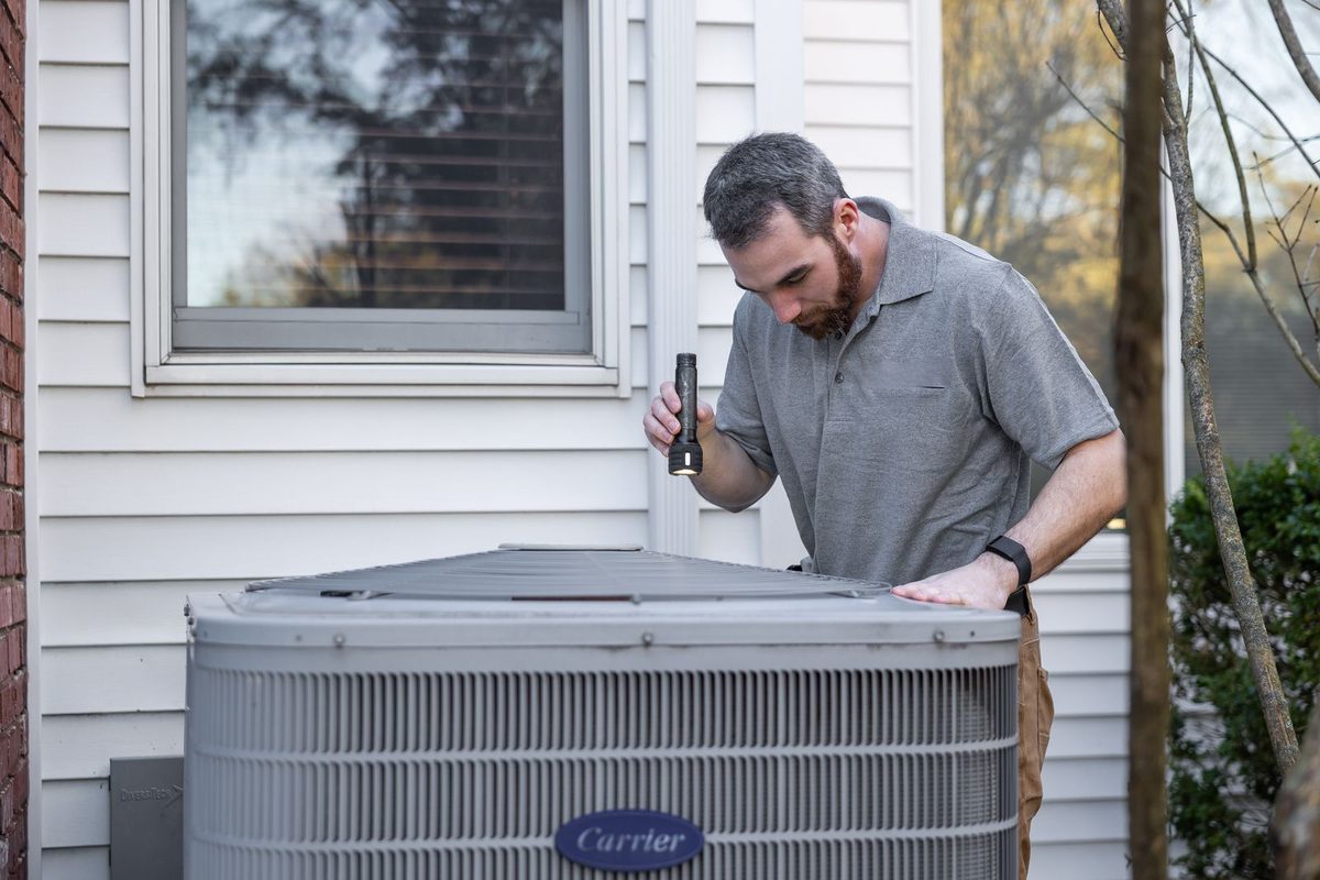 HVAC technician inspecting an outdoor air conditioning condenser unit beside a Dallas home